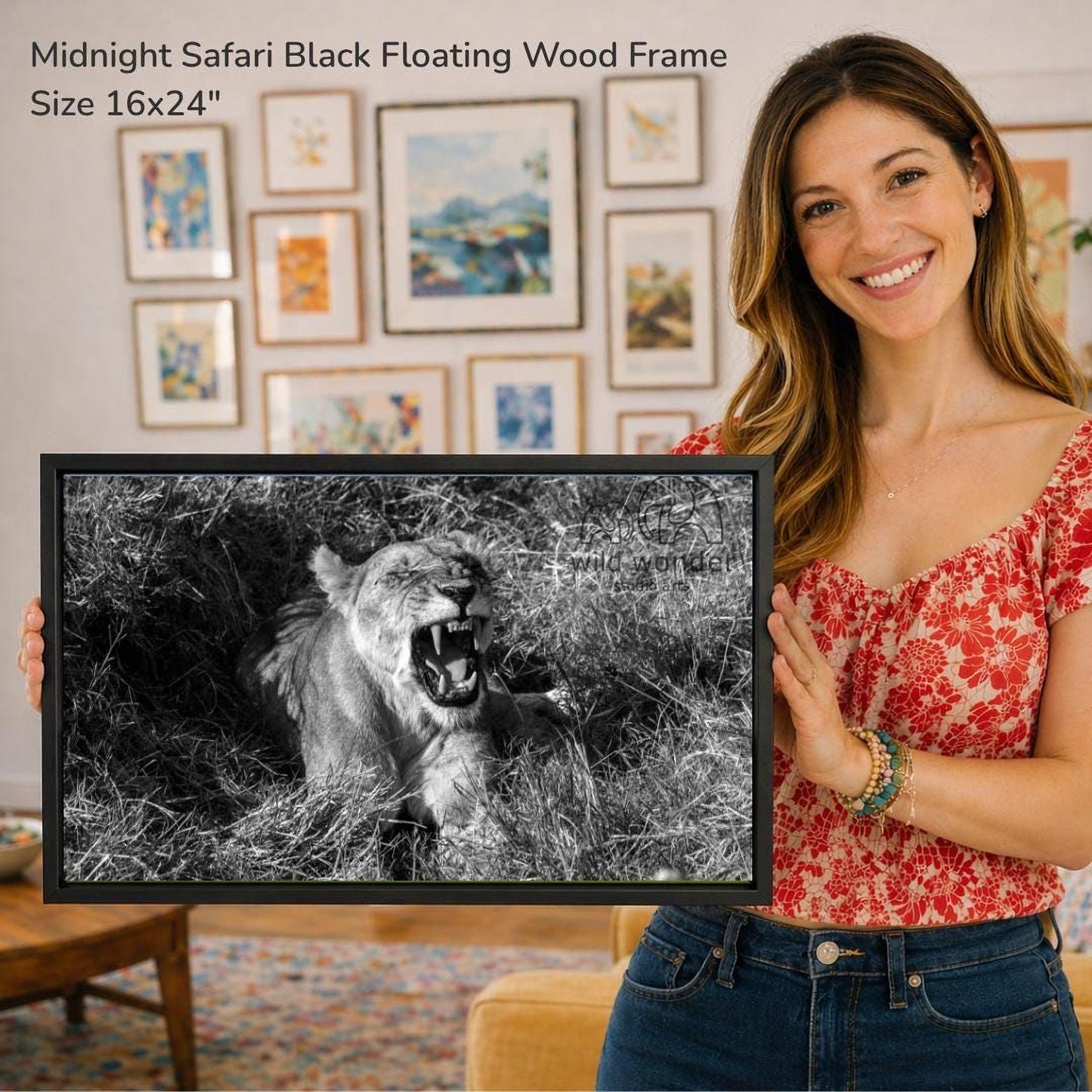 A woman is holding a framed photograph of a lion in a grassy field, with a smiling expression.