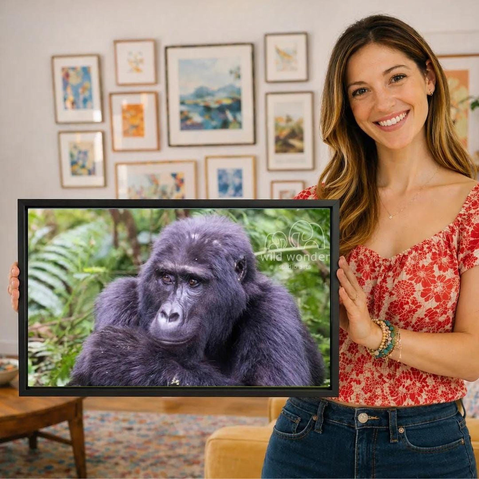 A woman is holding a framed photograph of a gorilla in front of a wall with various framed artworks.
