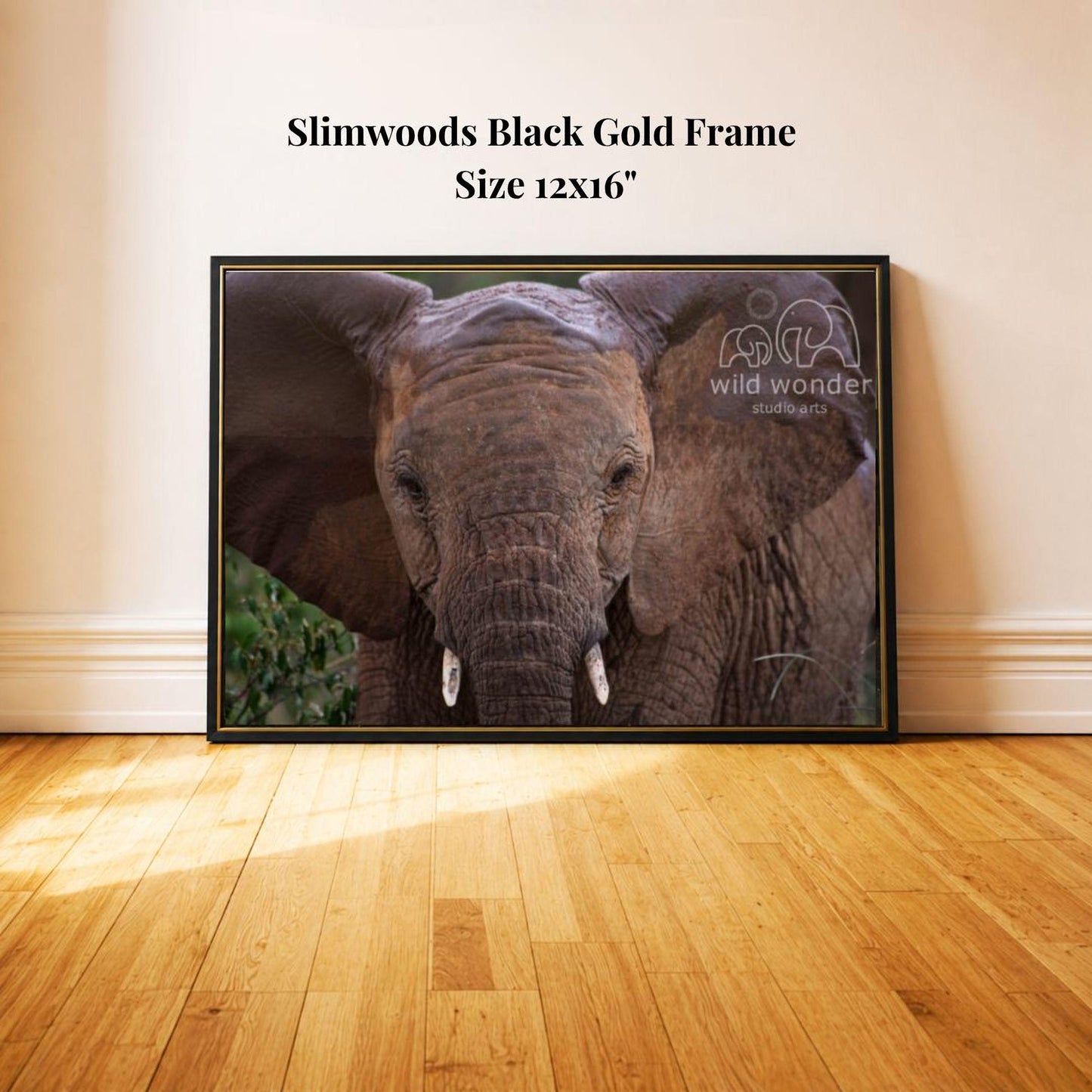 A framed photograph of an elephant is displayed on a wooden floor against a white wall.