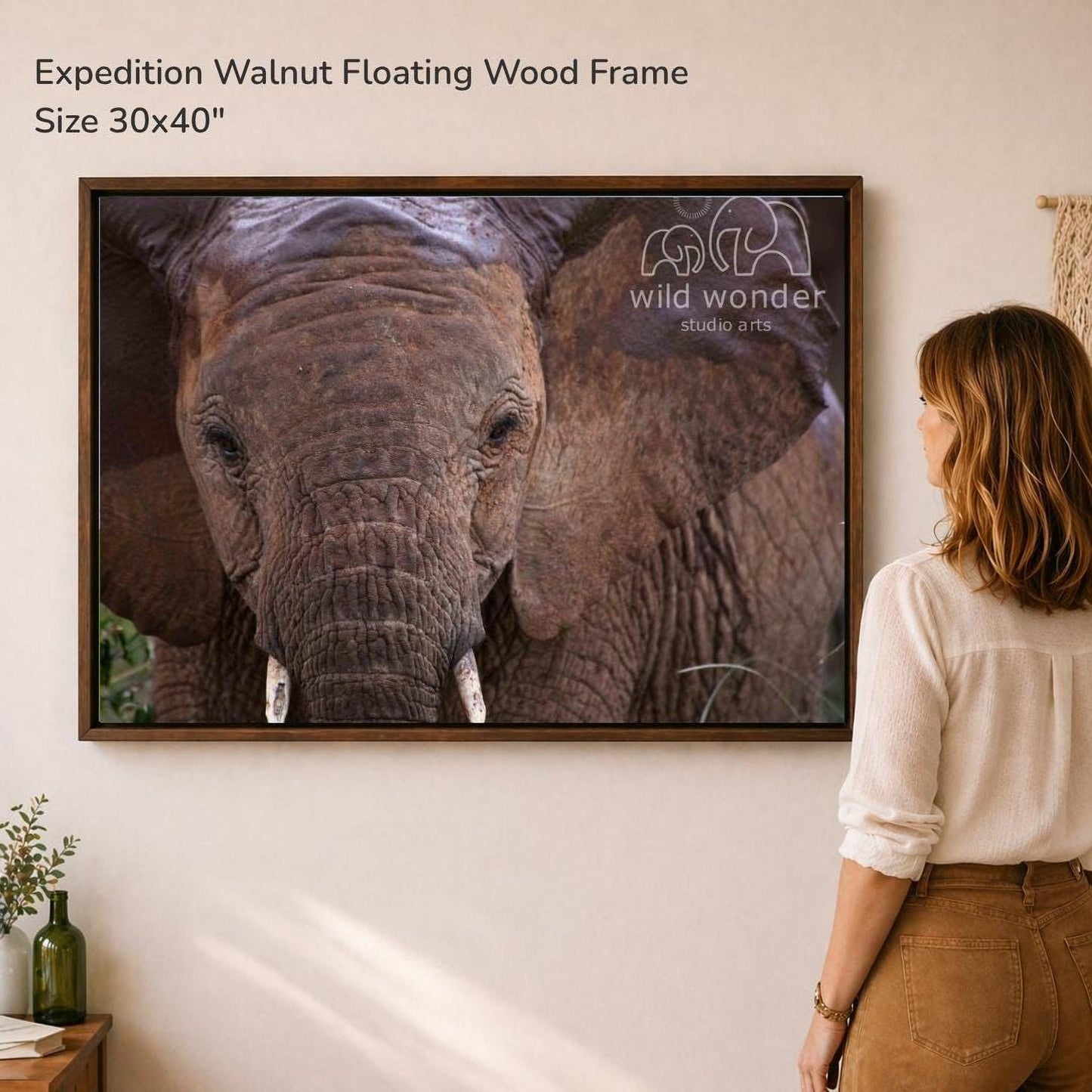 A woman is standing in front of a large framed photograph of an elephant, looking at it with interest.