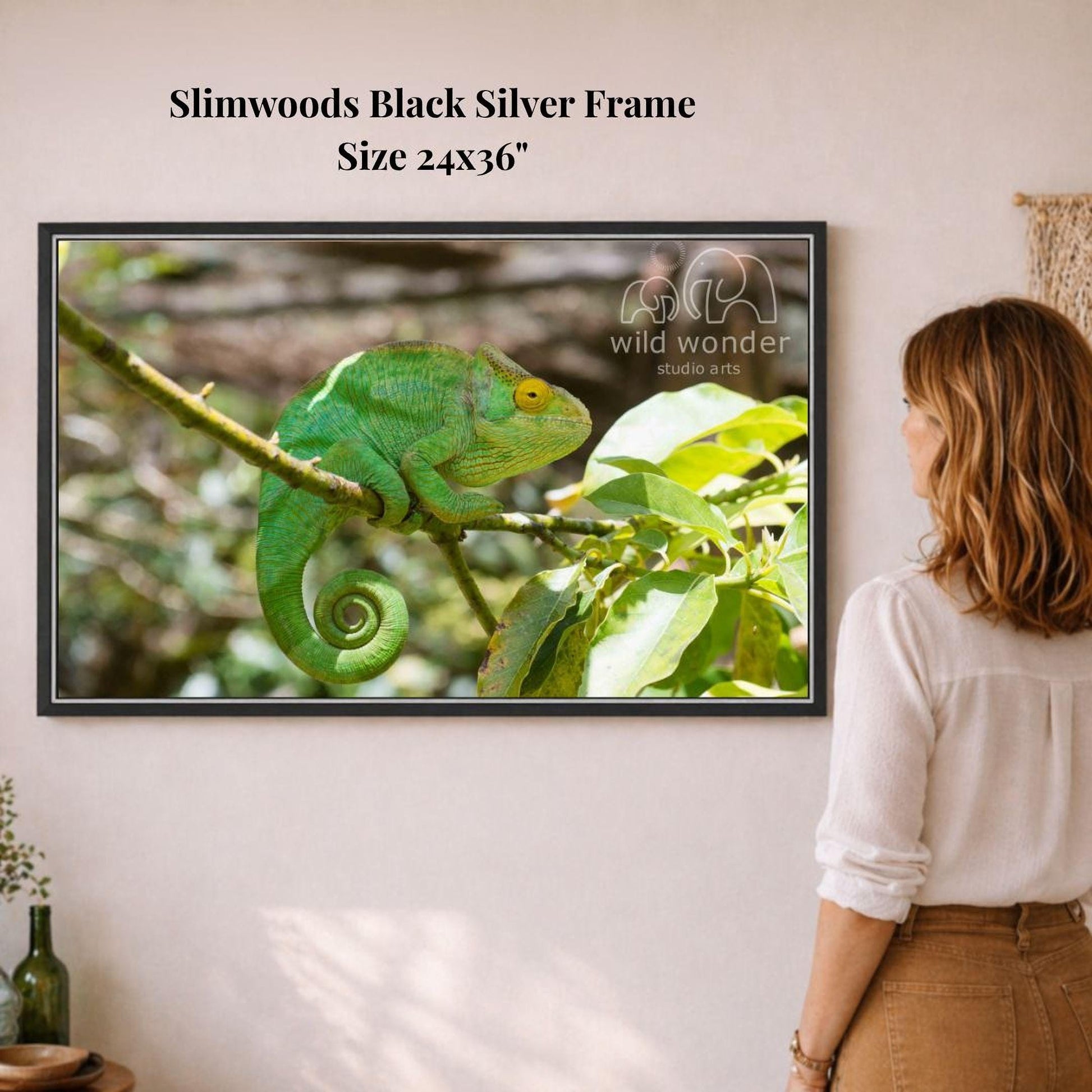 A woman is standing in front of a framed photograph of a green chameleon perched on a branch, observing the scene.