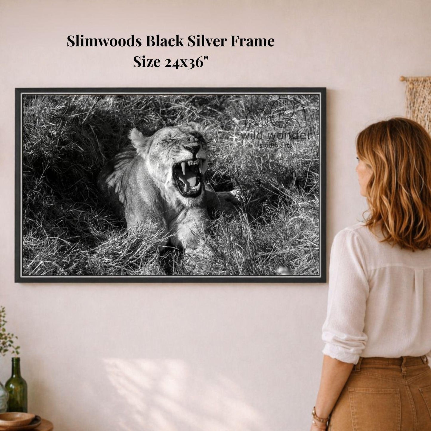 A woman is standing in front of a framed black and white photograph of a lion in a grassy field, which is hanging on a wall.