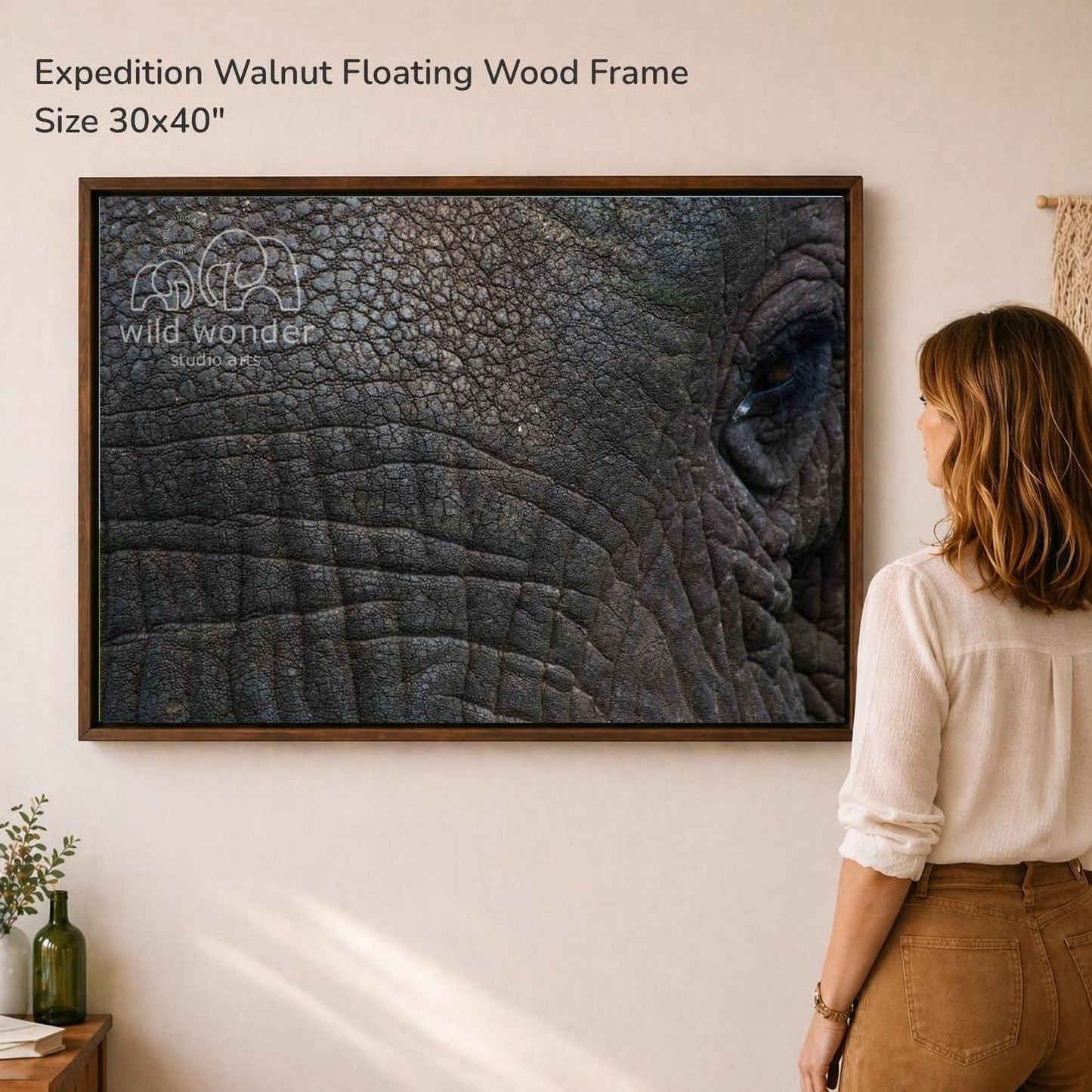 A woman is standing in front of a large framed photograph of an elephant's eye, looking at it with interest.