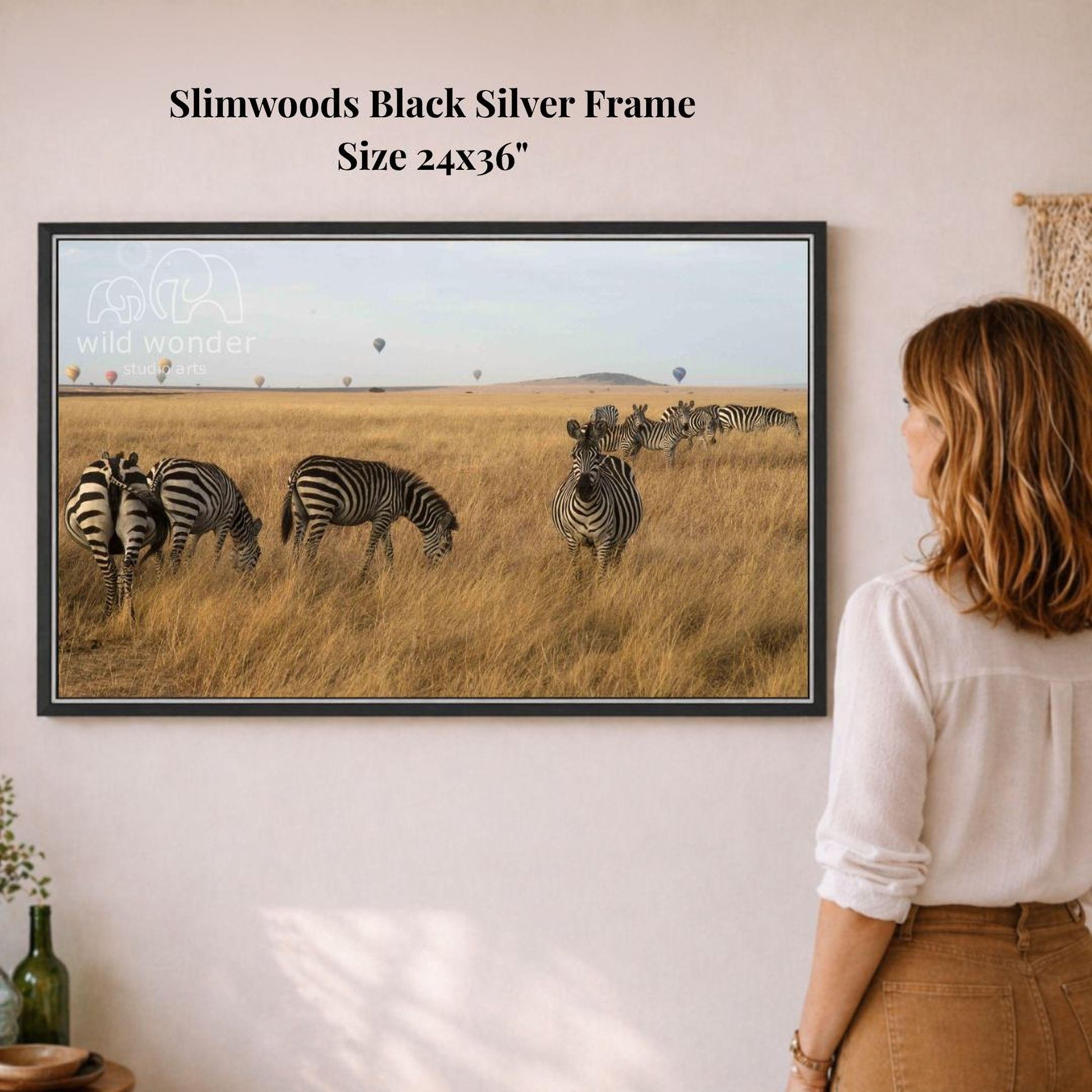 A woman is standing in front of a framed photograph of a group of zebras grazing in a grassy field.