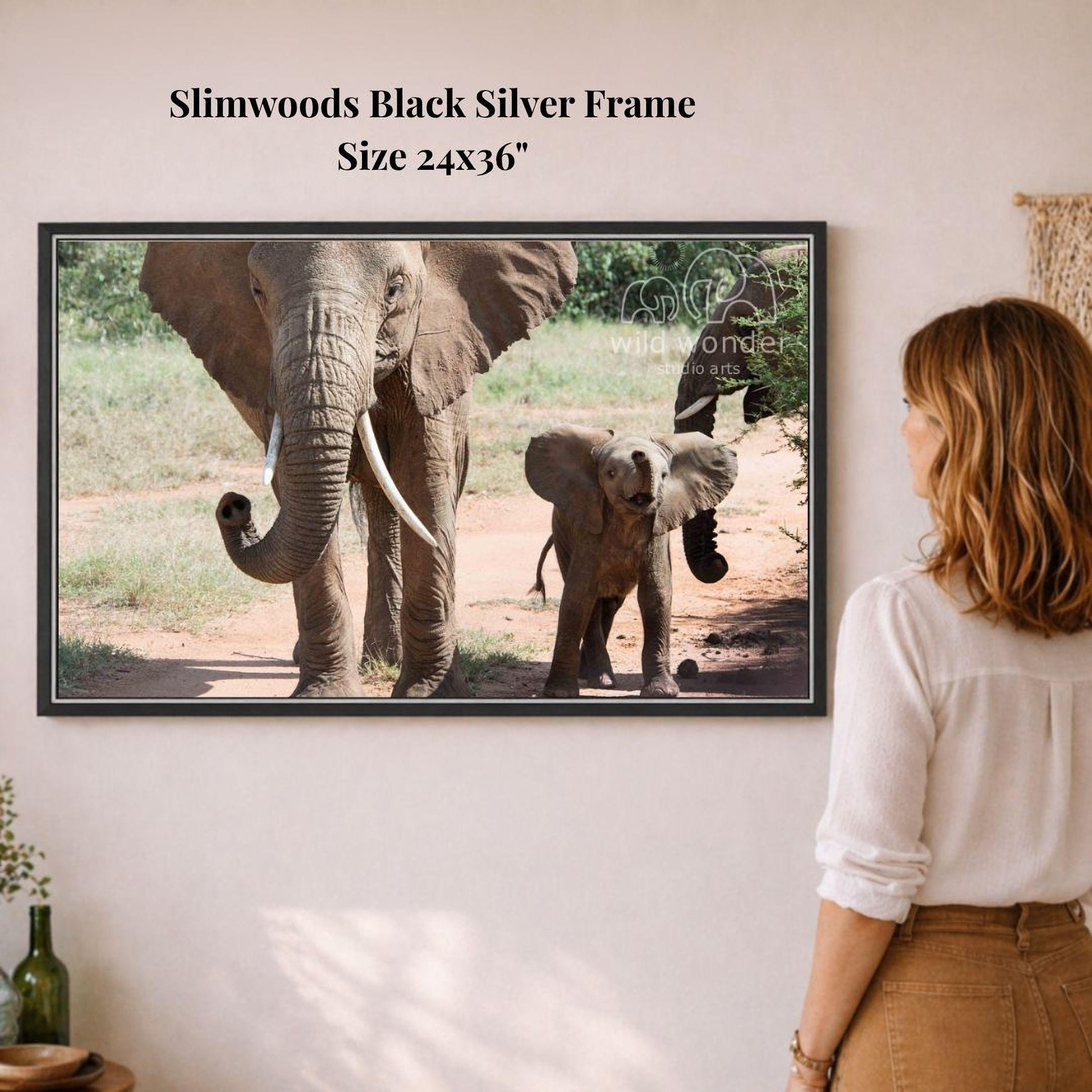 A woman is standing in front of a framed photograph of two elephants, one larger and one smaller, in a natural setting.