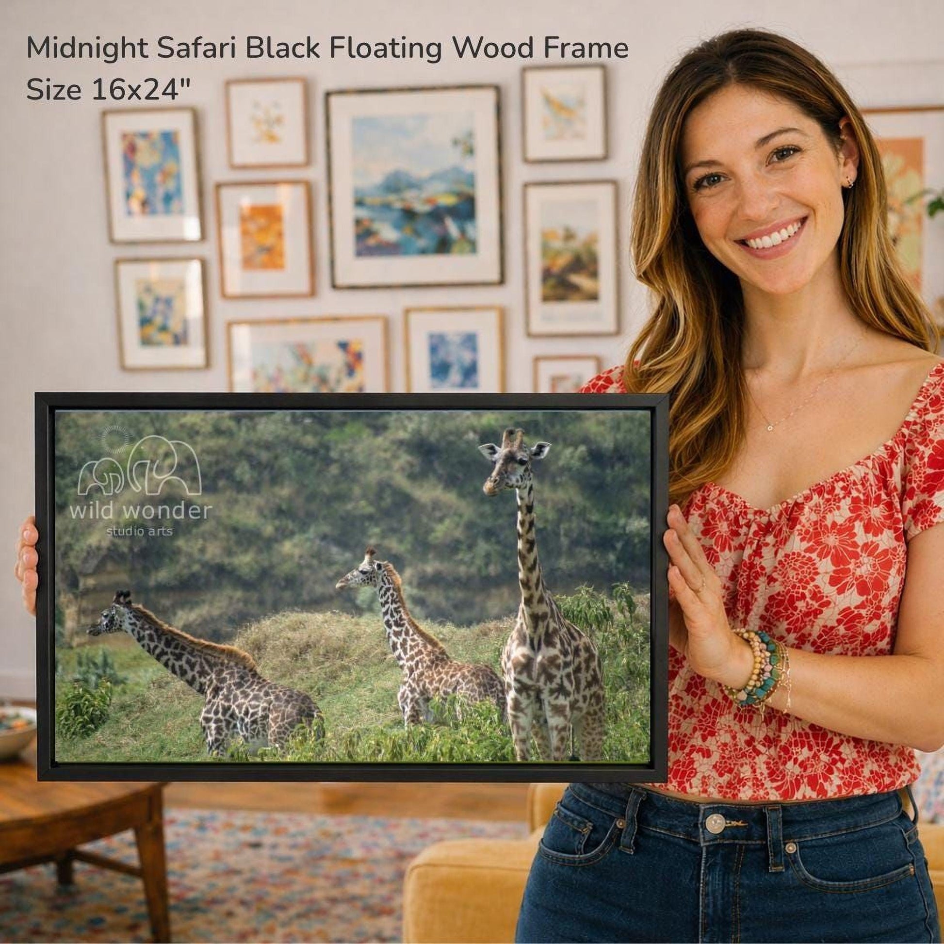 A woman is holding a framed photograph of three giraffes in a grassy field, with a smiling expression on her face.