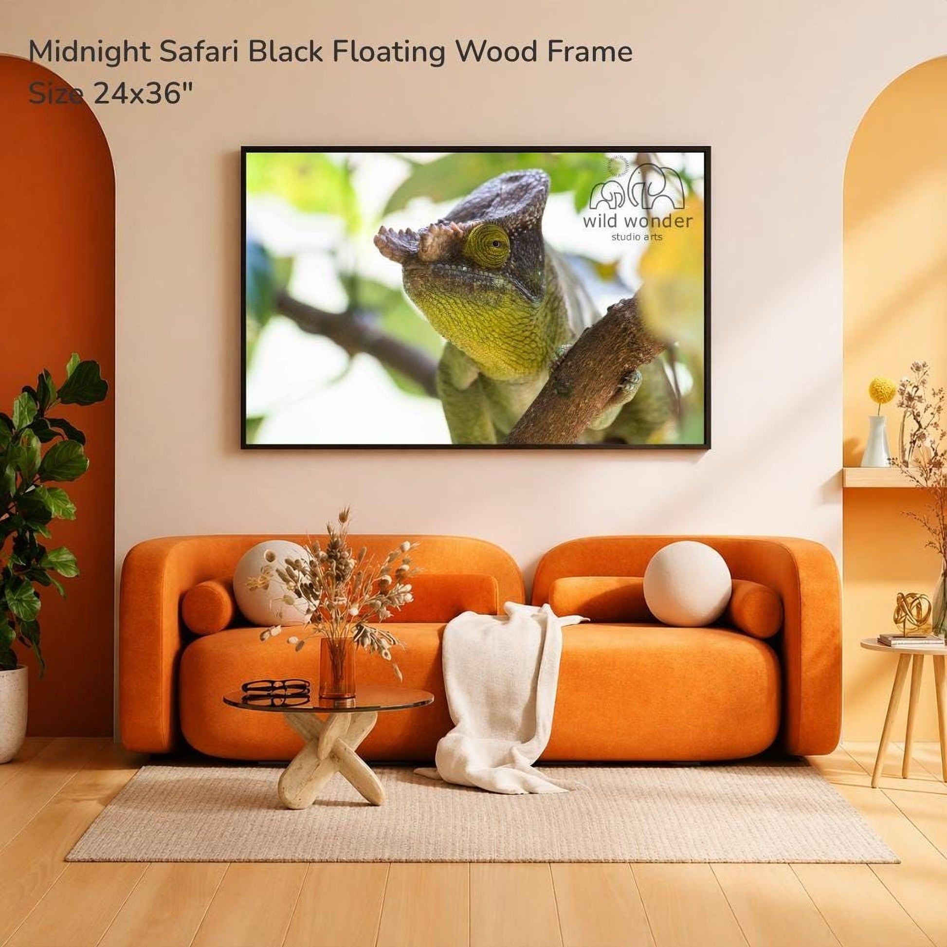a large black floating wood frame hanging on a wall, displaying a close-up of a chameleon. The frame is set against a beige wall, and the room has an orange sofa and a glass coffee table. There are also some decorative elements, such as a vase and a potted plant, adding to the cozy and inviting atmosphere of the space.