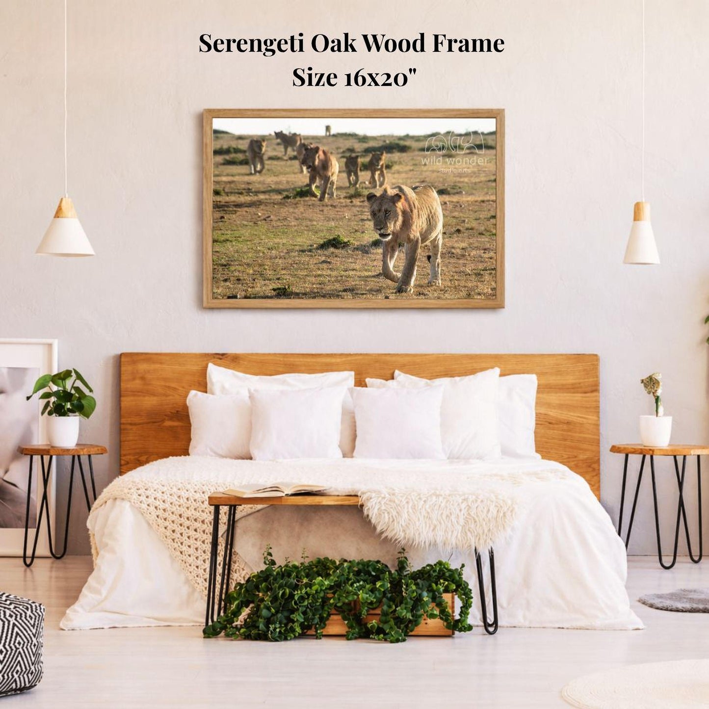a serene bedroom scene with a large framed photograph of a herd of animals, likely zebras, in a grassy field. The photograph is hanging on the wall above a bed with white bedding and pillows. The room has a wooden headboard and a wooden nightstand on each side of the bed, with a potted plant and a small plant on the nightstands. The overall atmosphere of the room is calm and peaceful, with the natural elements of the animals and the grassy field creating a sense of tranquility.