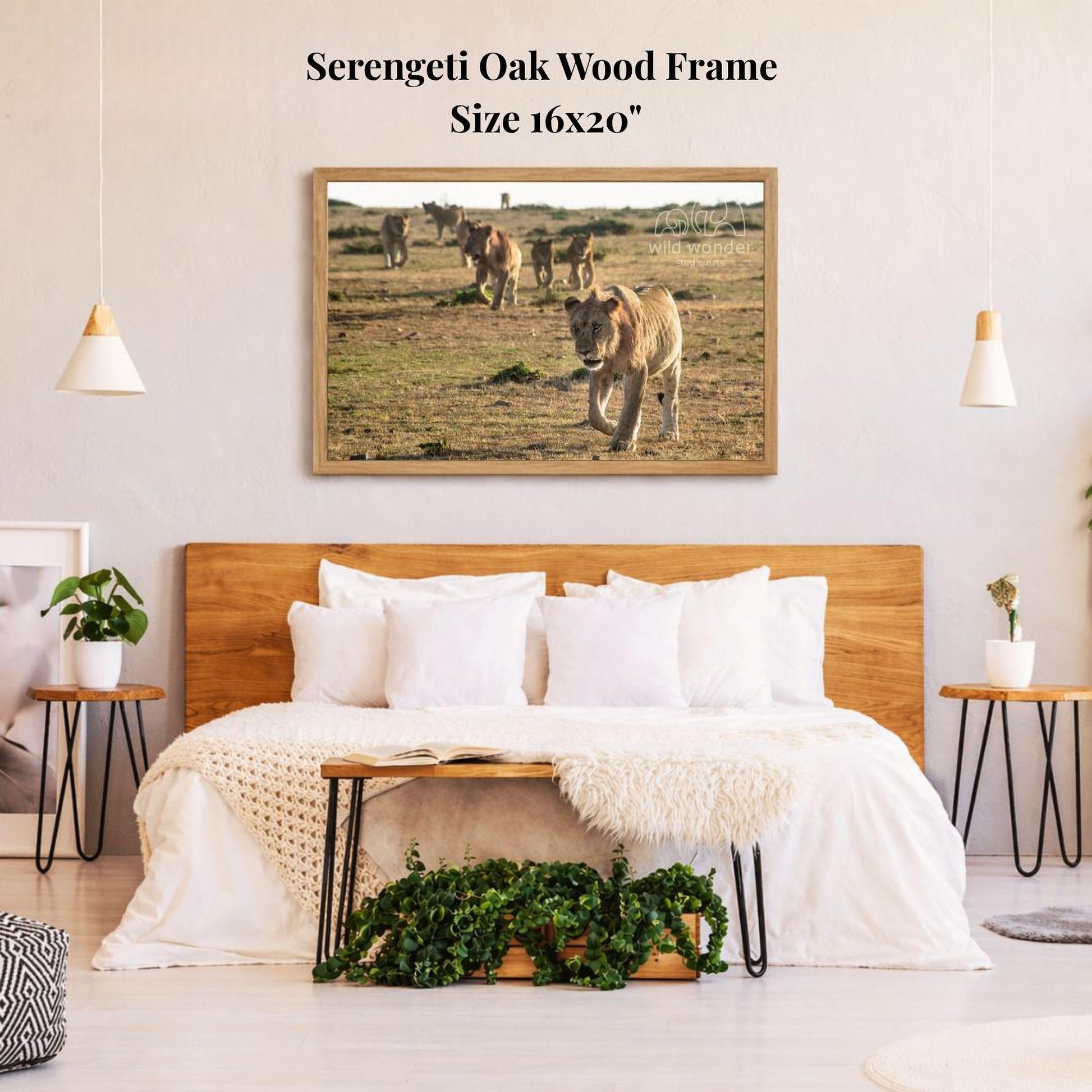a serene bedroom scene with a large framed photograph of a herd of animals, likely zebras, in a grassy field. The photograph is hanging on the wall above a bed with white bedding and pillows. The room has a wooden headboard and a wooden nightstand on each side of the bed, with a potted plant and a small plant on the nightstands. The overall atmosphere of the room is calm and peaceful, with the natural elements of the animals and the grassy field creating a sense of tranquility.