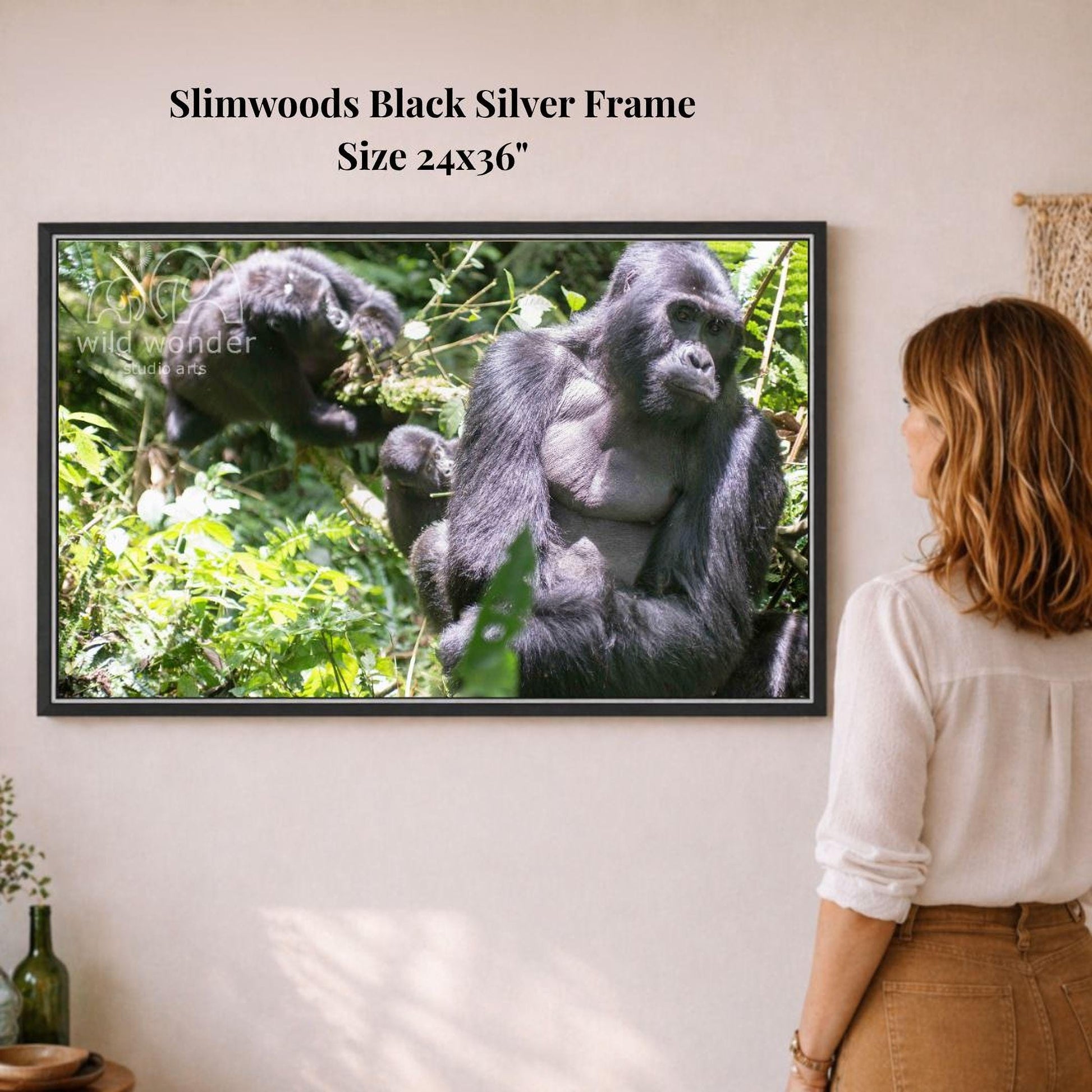 A woman is standing in front of a framed photograph of two gorillas in a lush, green forest setting.
