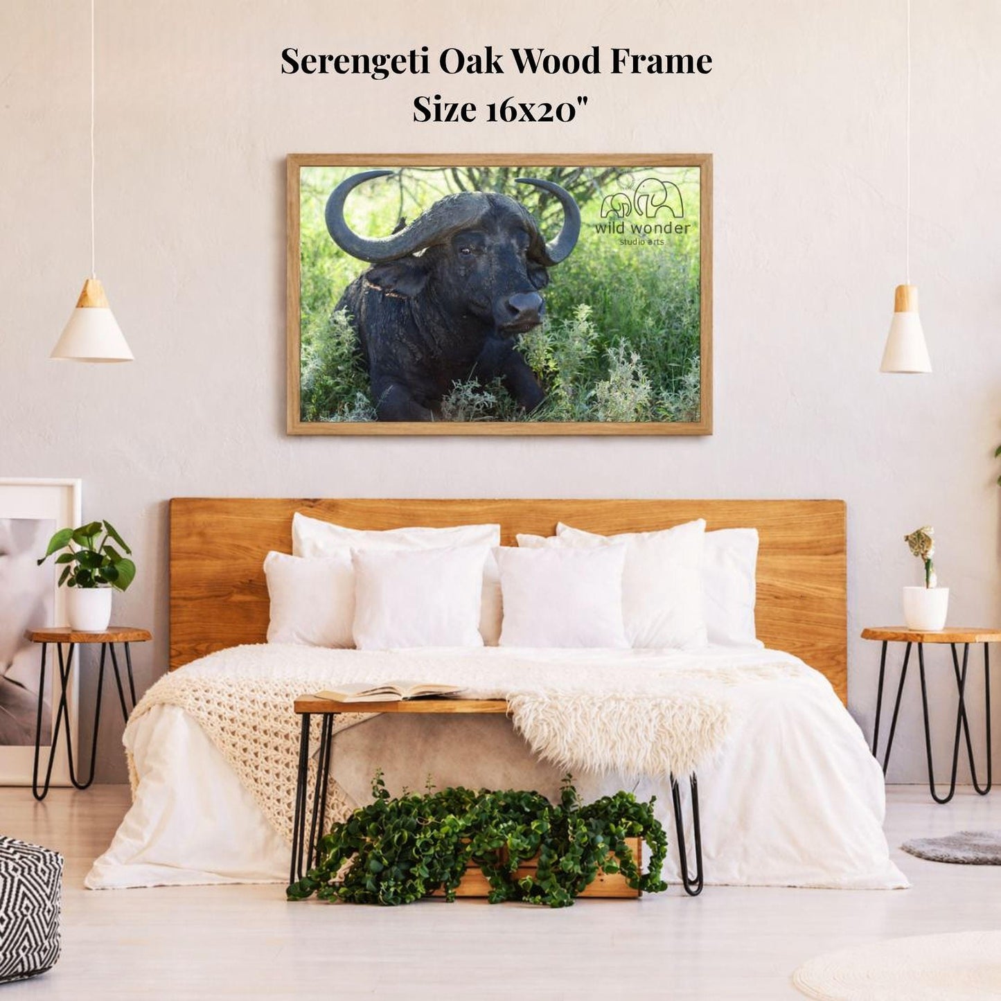 a serene bedroom scene with a large framed picture of a horned animal, likely a buffalo or ox, hanging on the wall above a bed with white bedding. The room has a wooden headboard and a wooden nightstand on each side of the bed, with a potted plant and a small plant on the nightstands. The overall atmosphere of the room is calm and serene, with the natural elements of the plants and the wooden furniture complementing the peaceful image of the animal.