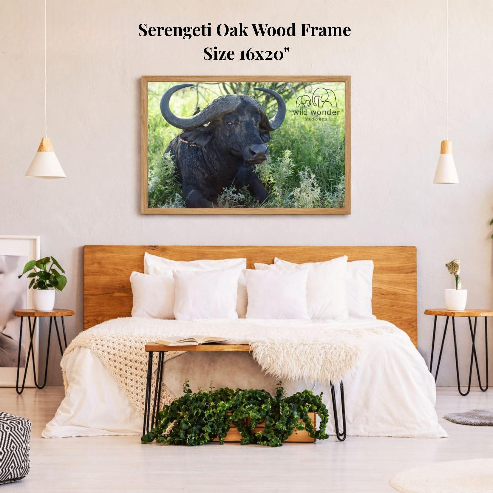 a serene bedroom scene with a large framed picture of a horned animal, likely a buffalo or ox, hanging on the wall above a bed with white bedding. The room has a wooden headboard and a wooden nightstand on each side of the bed, with a potted plant and a small plant on the nightstands. The overall atmosphere of the room is calm and serene, with the natural elements of the plants and the wooden furniture complementing the peaceful image of the animal.