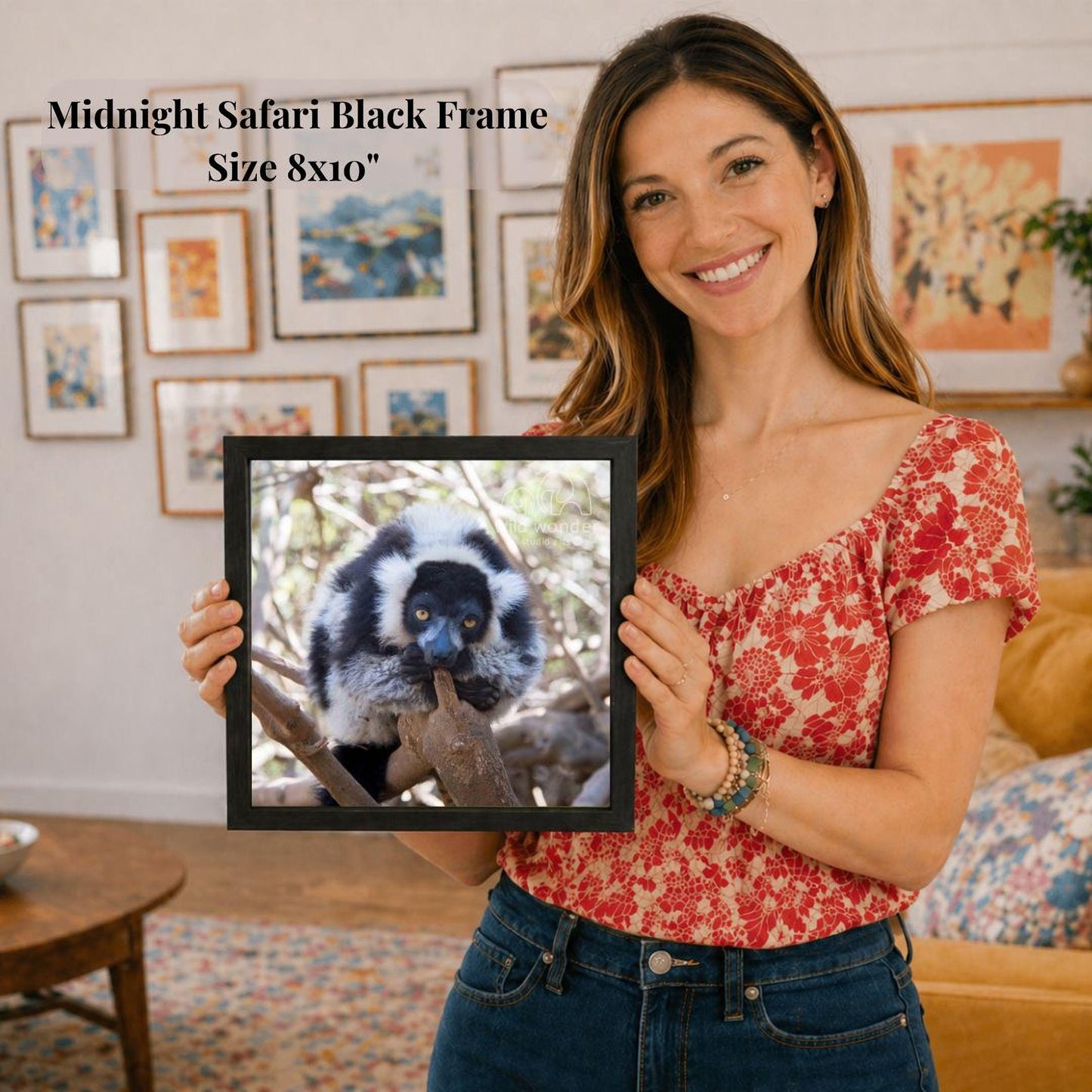 A woman is holding a framed picture of a lemur in a forest setting, with a smiling expression on her face.