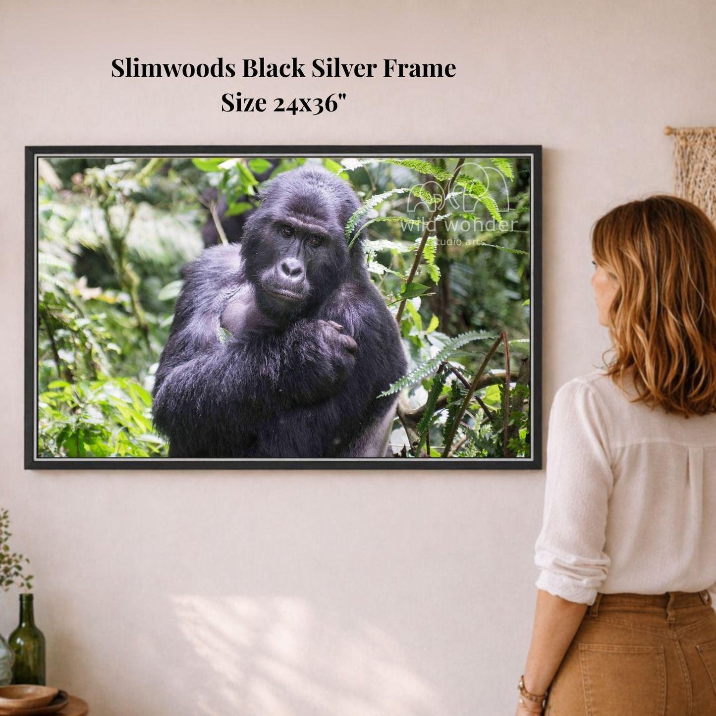 A woman is standing in front of a framed photograph of a gorilla in a lush, green forest environment.