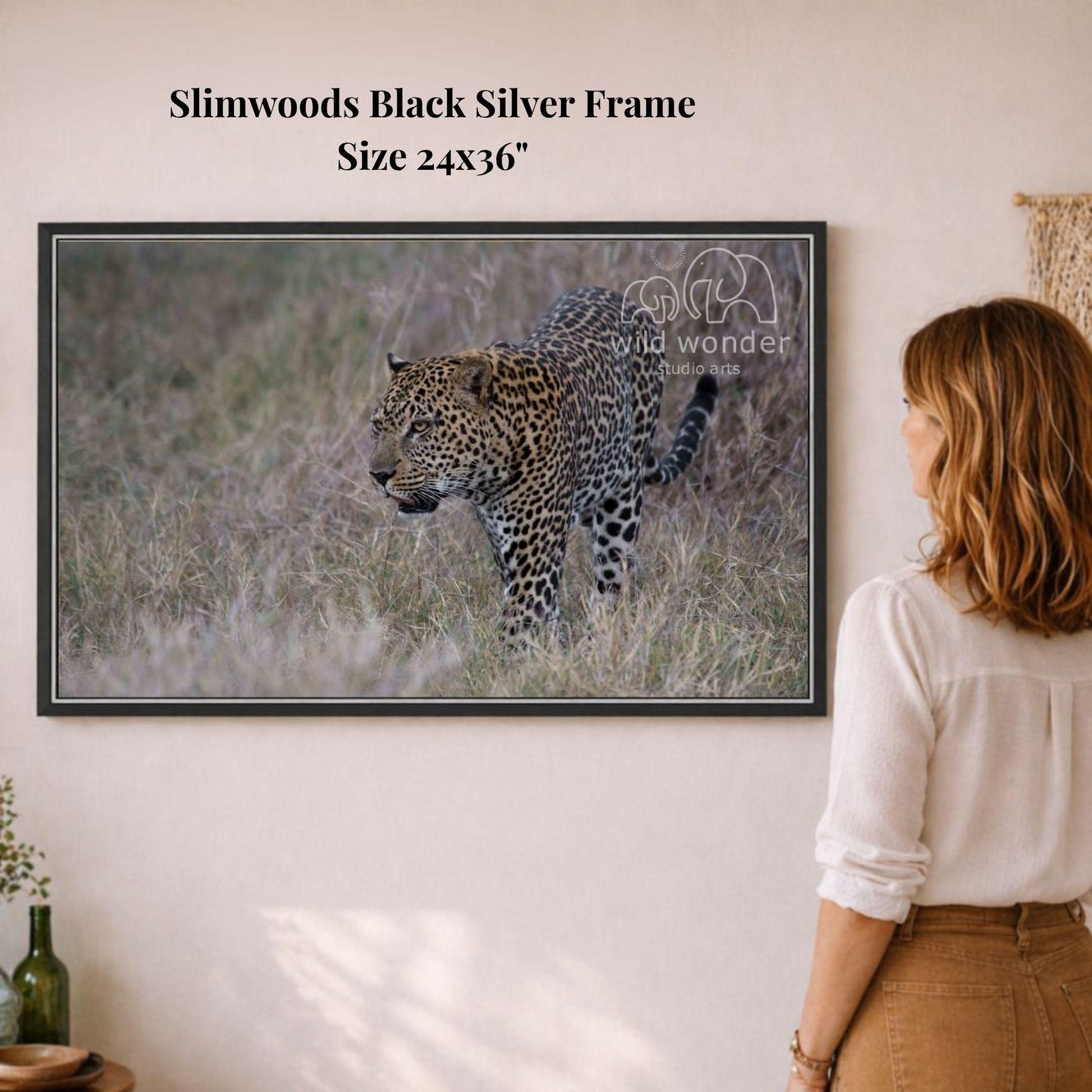 A woman is standing in front of a framed photograph of a leopard in a grassy field, observing the animal.