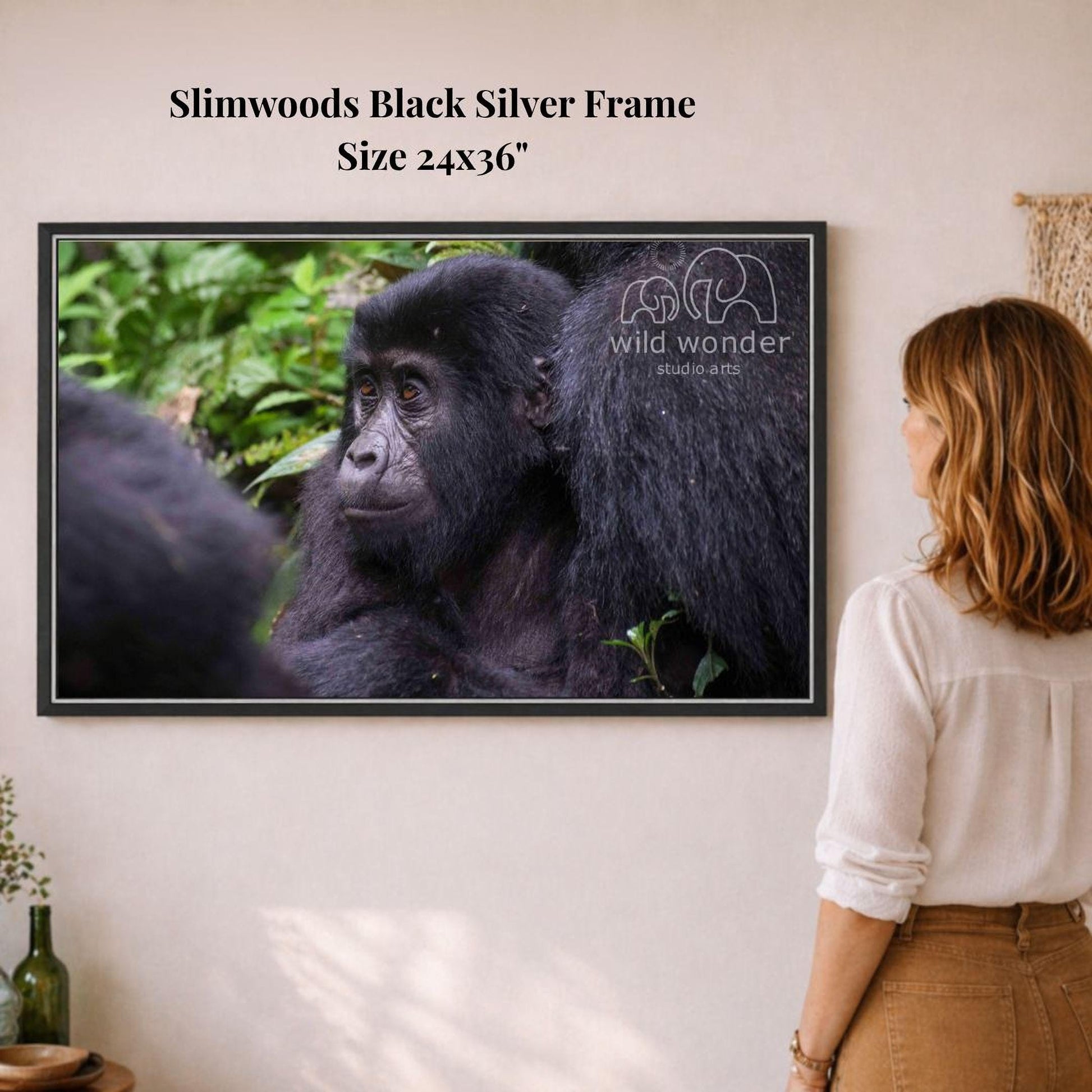 A woman is standing in front of a framed photograph of a black gorilla, looking at it with interest.