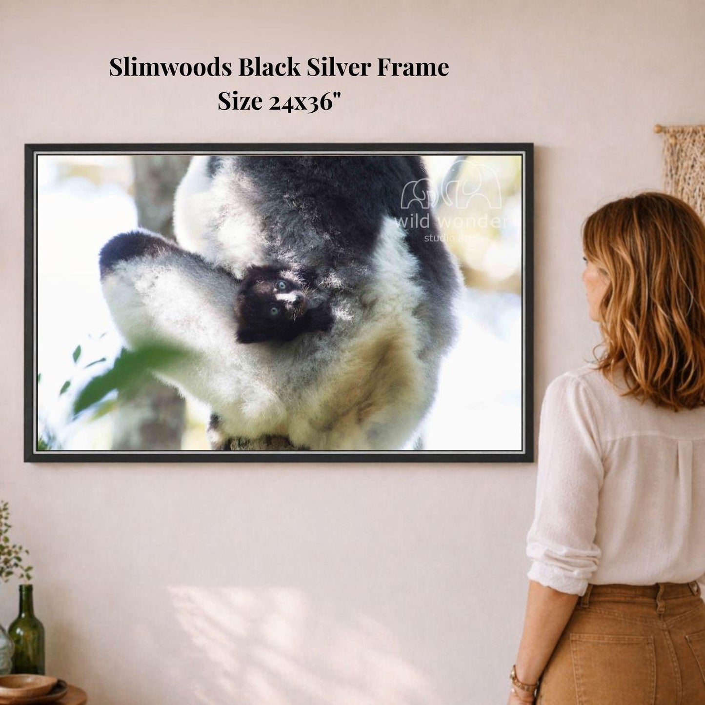 A woman is standing in front of a framed photograph of a black and white animal, likely a bird or a rodent, in a natural setting.