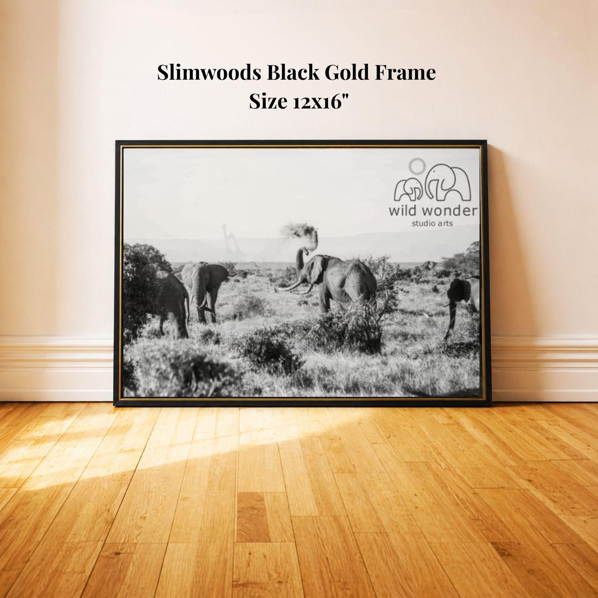 A black and white photograph of three elephants in a field, with a framed print of the same image displayed on a wall.