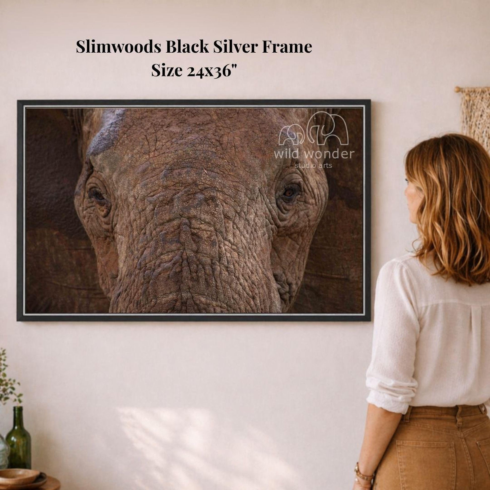 A woman is standing in front of a framed photograph of an elephant, looking at it with interest.