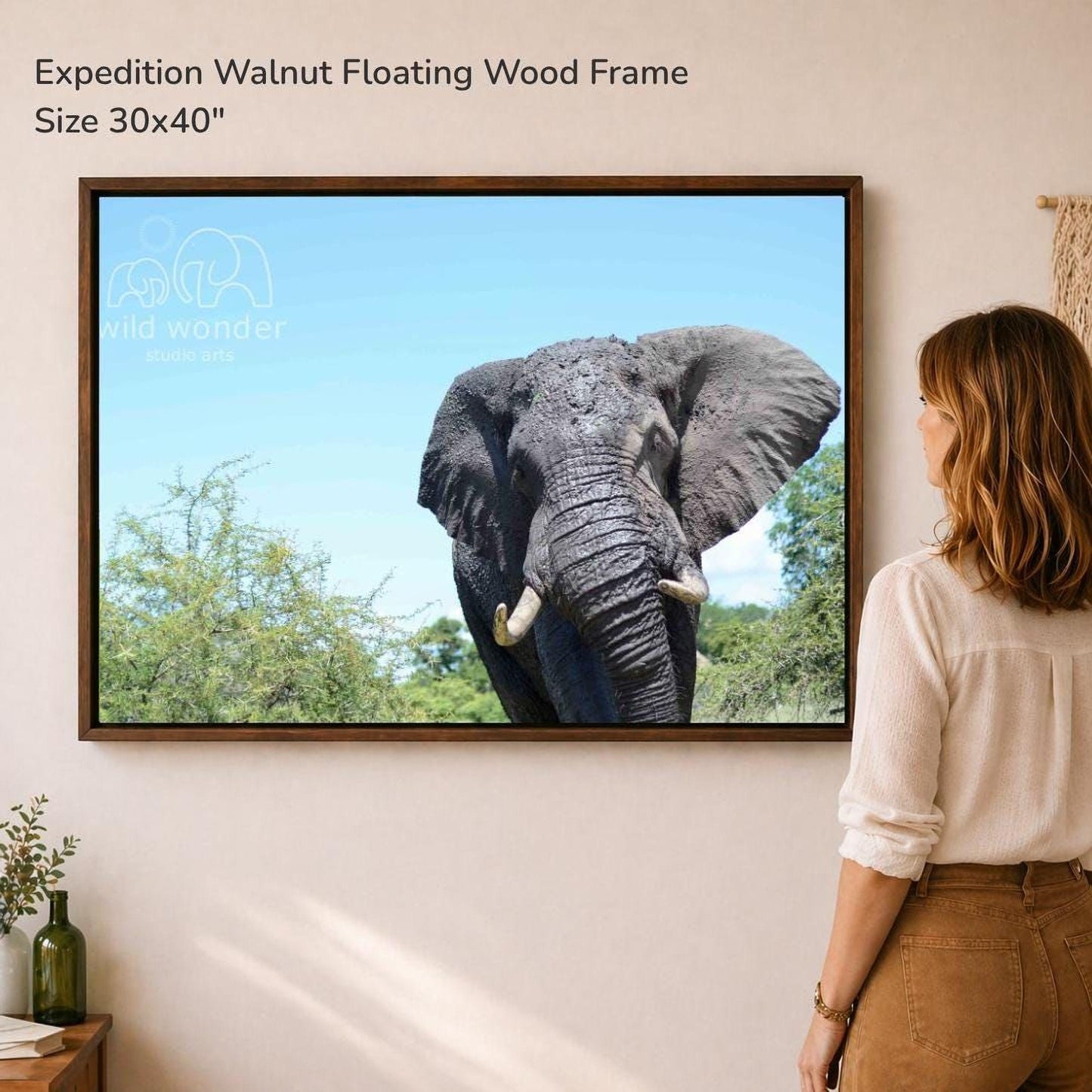 A woman is standing in front of a large framed photograph of an elephant, looking at the artwork on the wall.