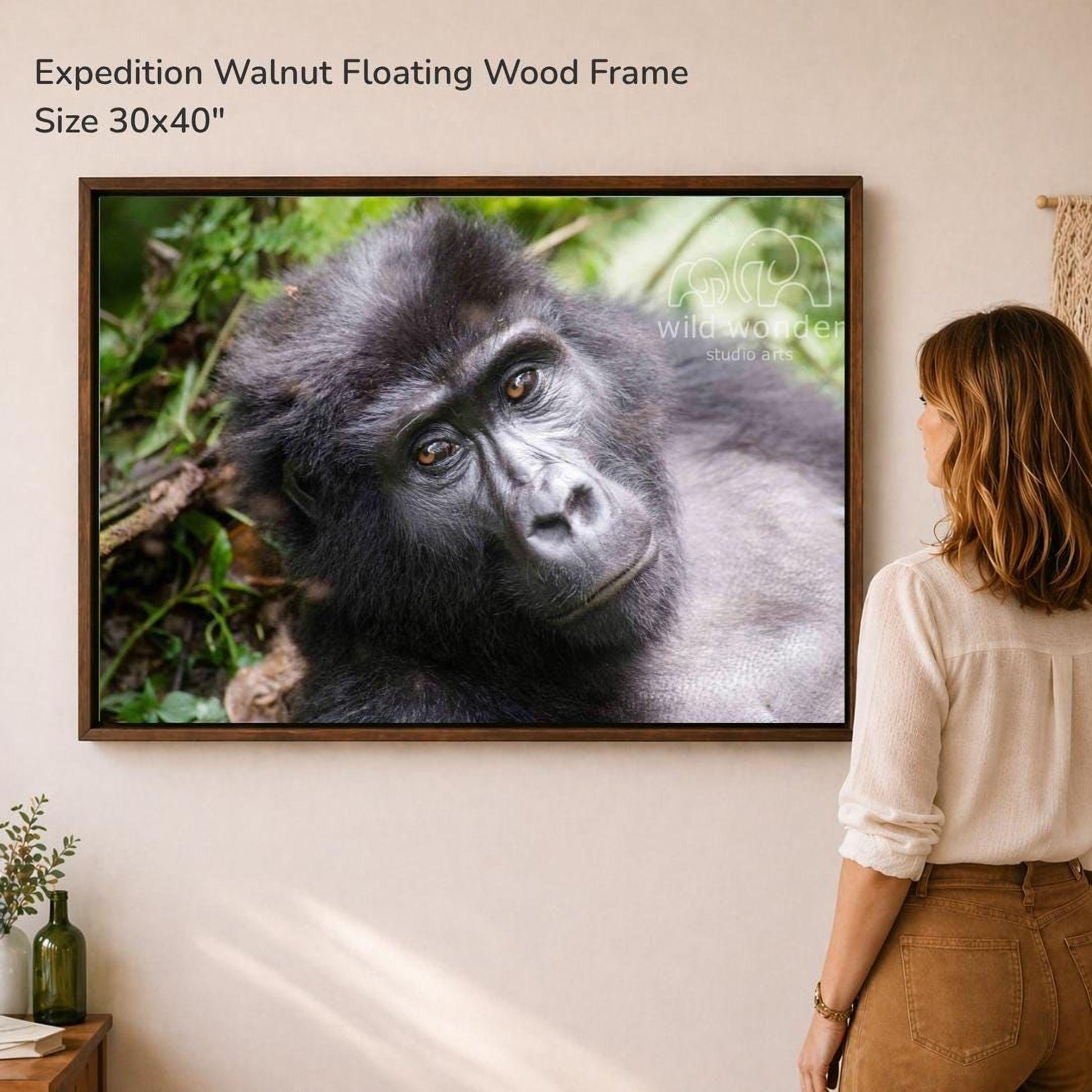 A woman is standing in front of a large framed photograph of a gorilla, looking at the artwork on the wall.