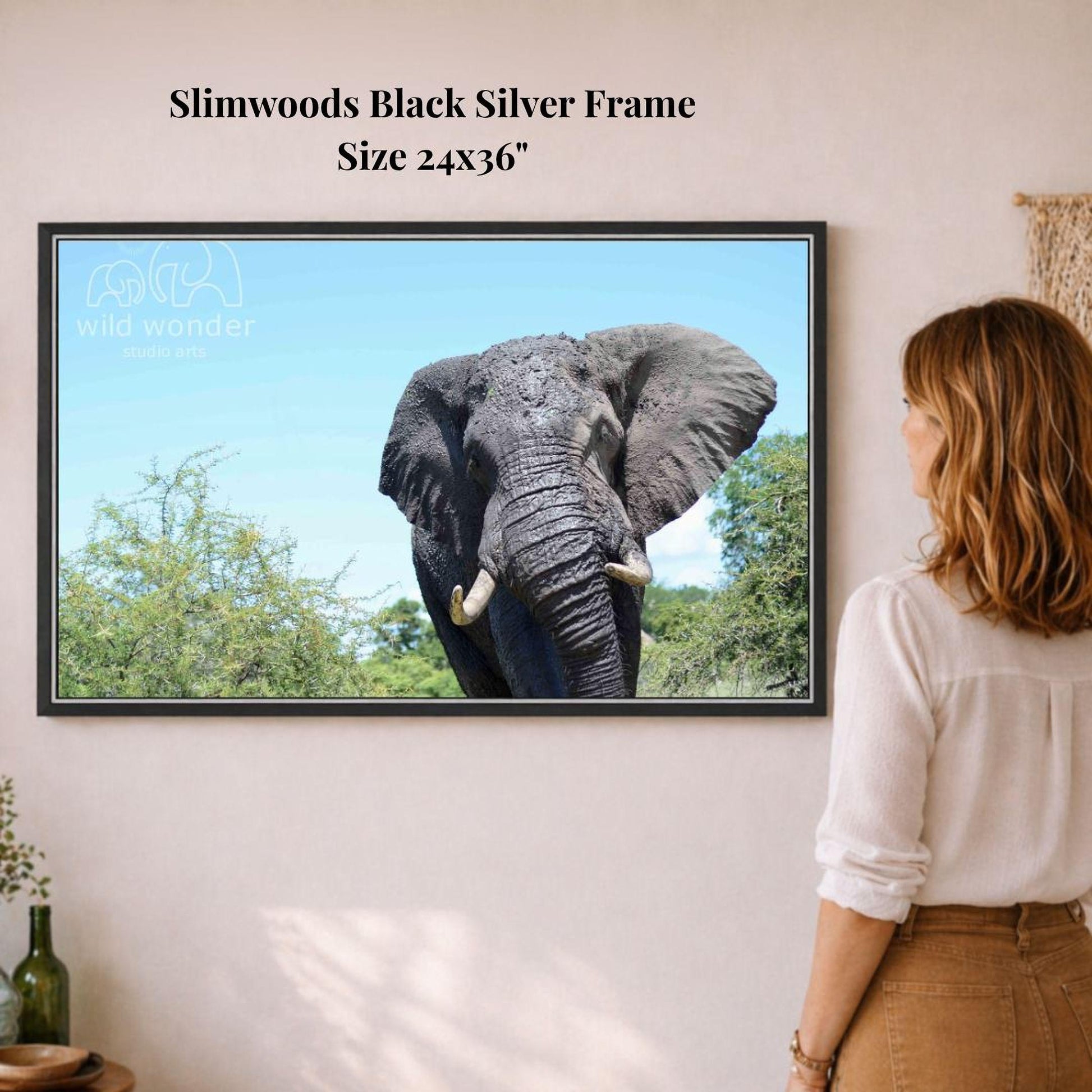 A woman is standing in front of a framed photograph of an elephant, looking at it with interest.