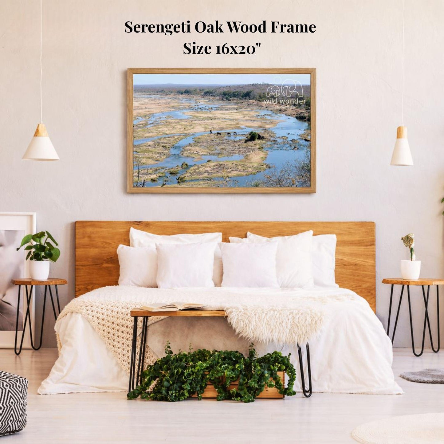 a serene bedroom setting with a large, 16x20" framed picture of a river and forest hanging on the wall above a bed with white bedding and a wooden headboard.