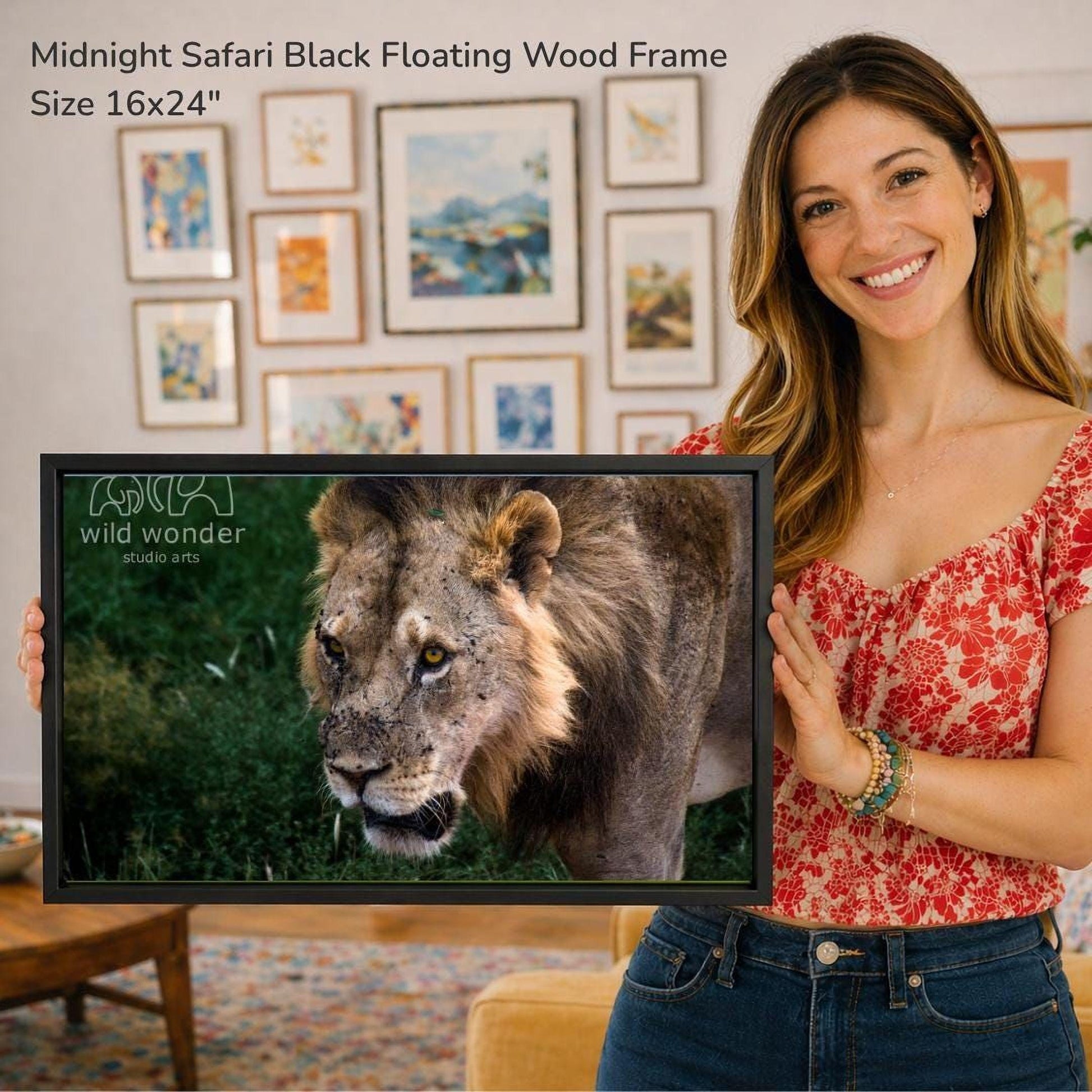 A woman is holding a framed photograph of a lion in front of a wall with various framed artworks.
