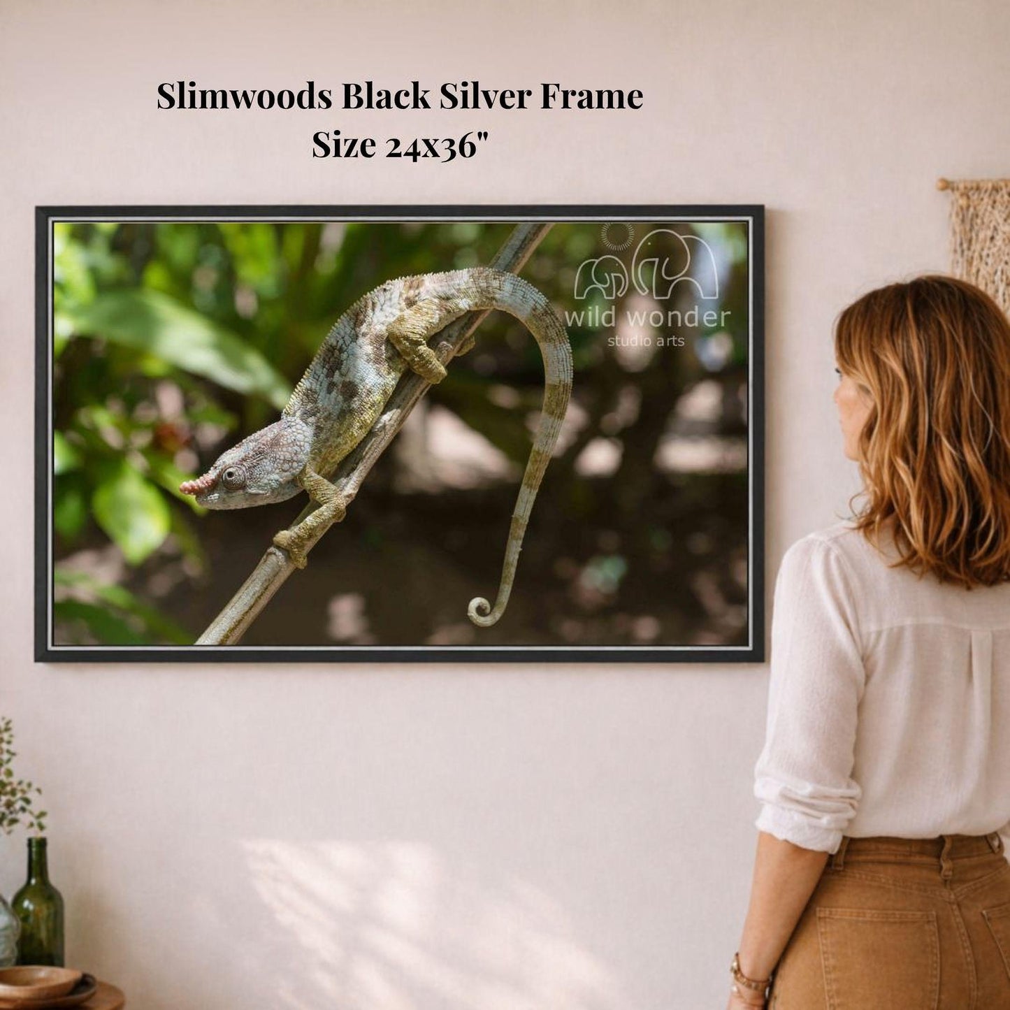 A woman is standing in front of a framed photograph of a chameleon on a branch, observing the artwork.